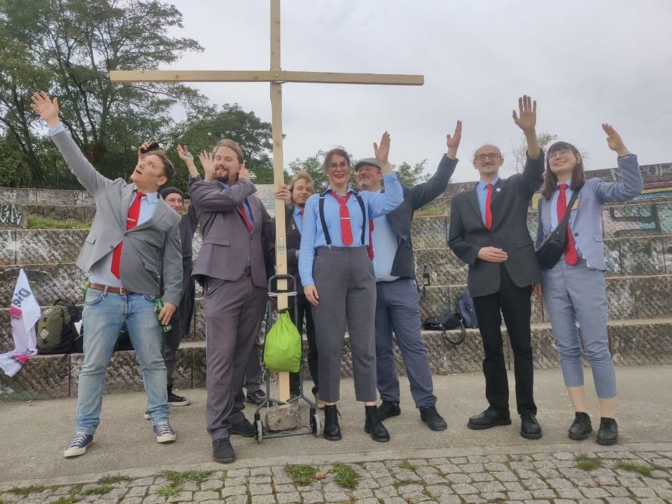 Zu sehen ist eine Gruppe von Mitgliedern der Partei Die PARTEI, die mit einem großen Kreuz posieren.